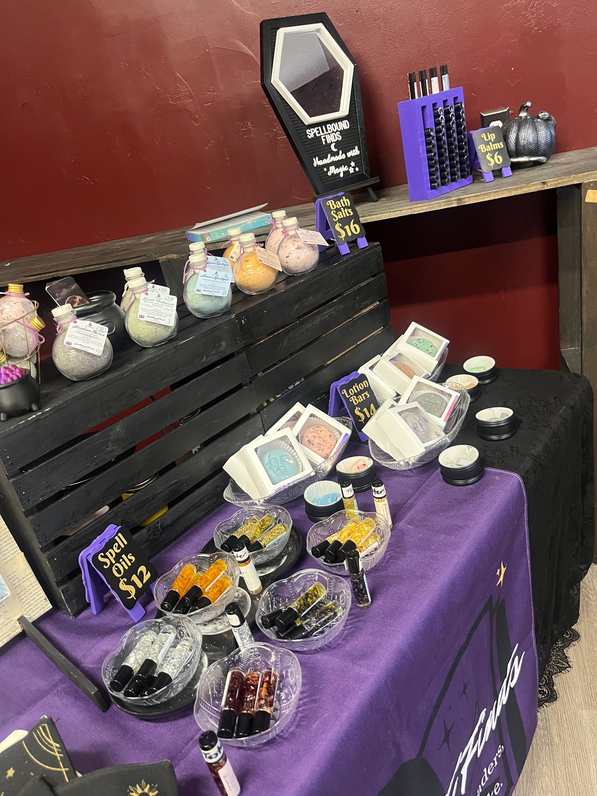 Purple-covered display table with assorted jewelry and small gift items on black shelves and trays