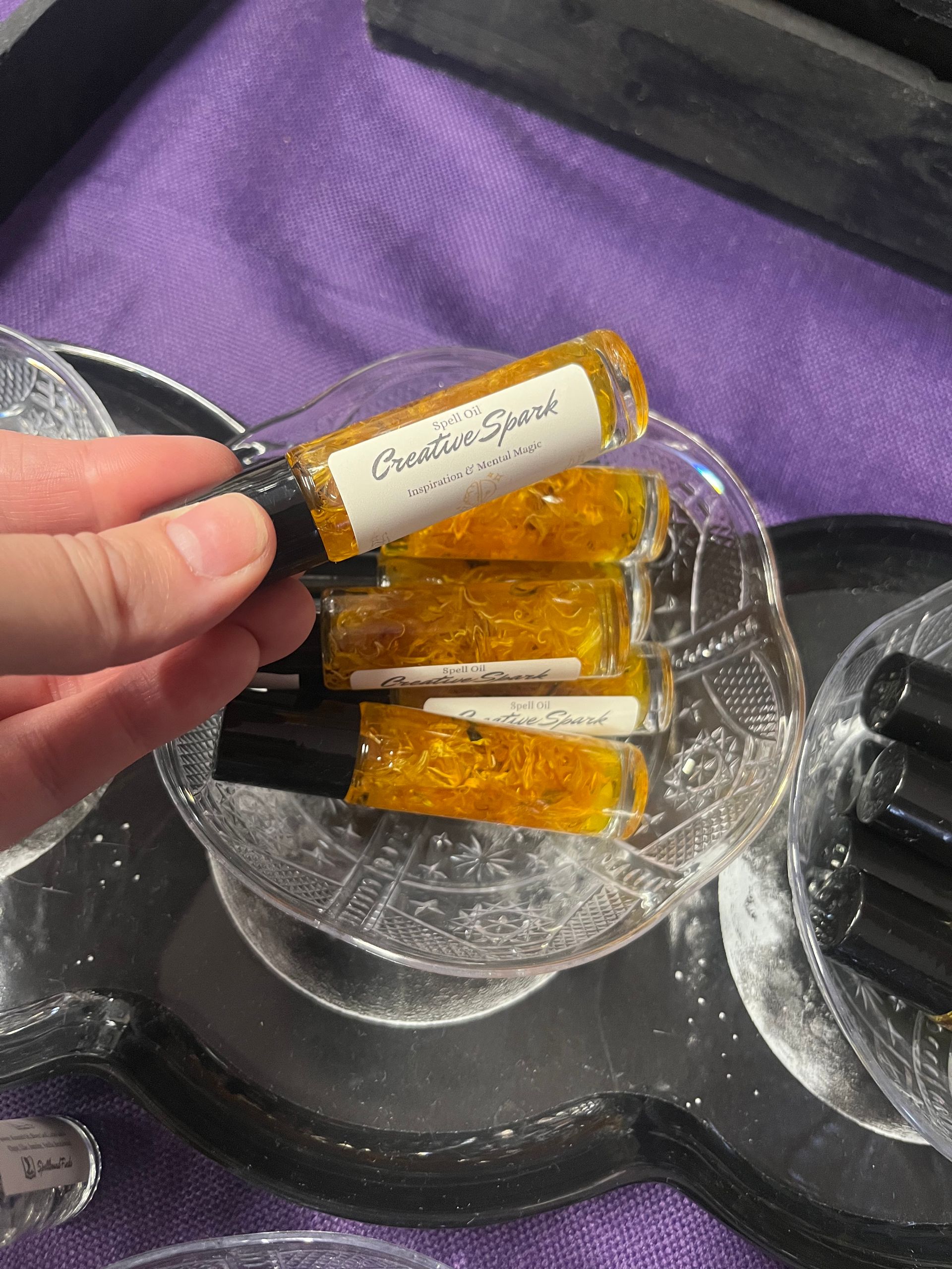 Hand holding amber jar candles on a silver tray over a purple fabric background