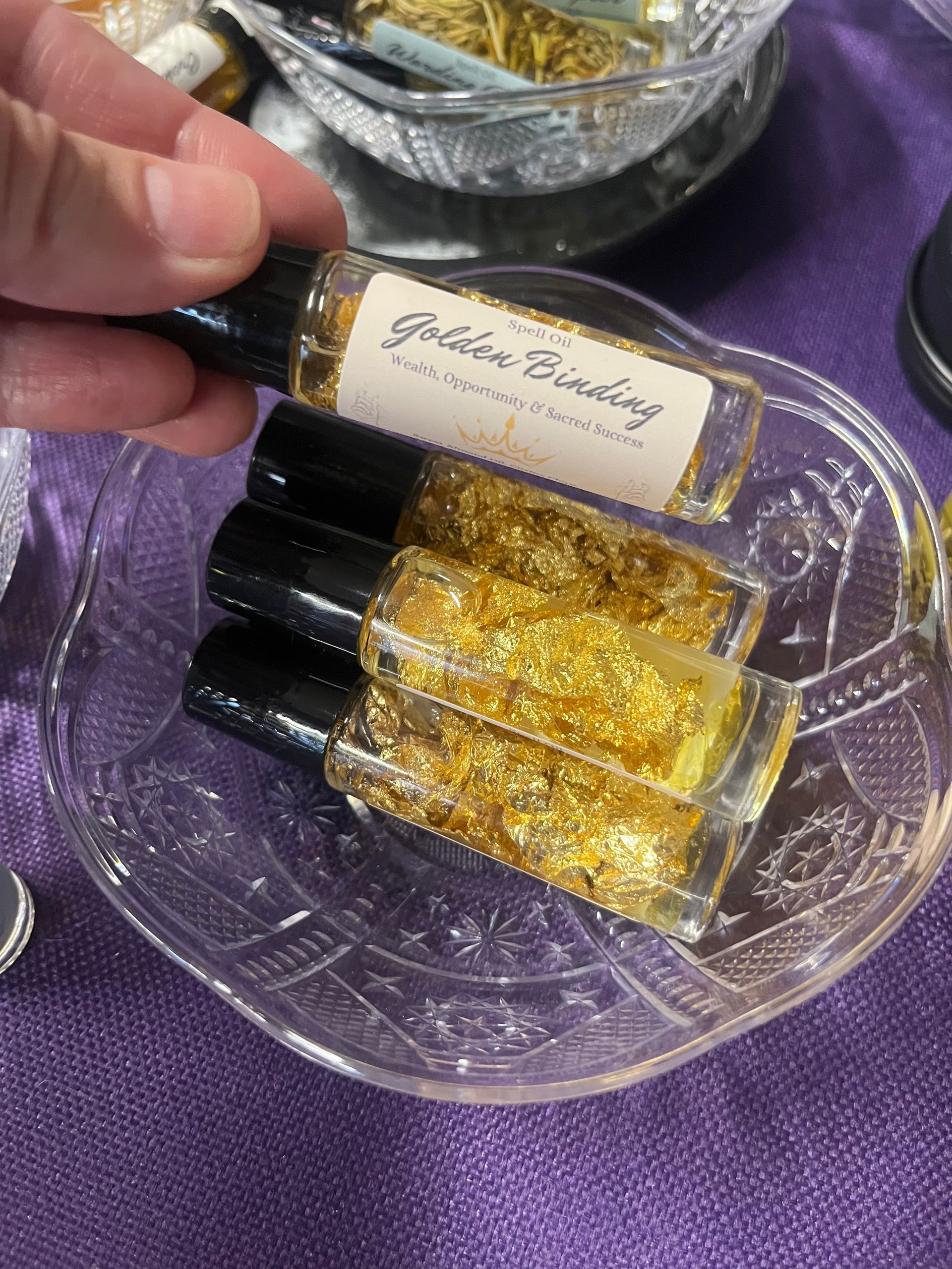 Hand holding small gold-glitter perfume vials in a clear tray on purple fabric
