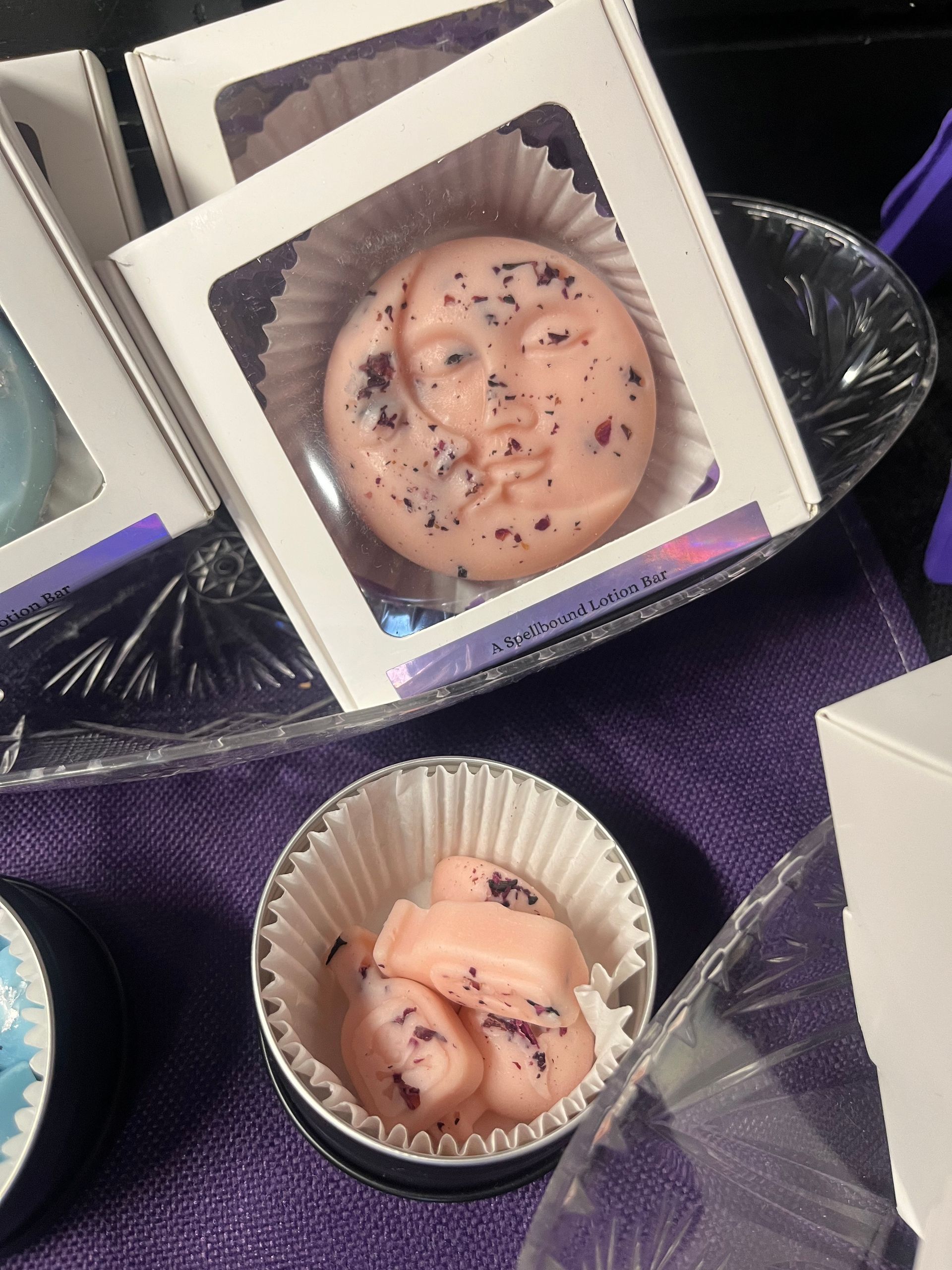 Small frosted cupcakes in white boxes, topped with chocolate sprinkles and purple drizzle