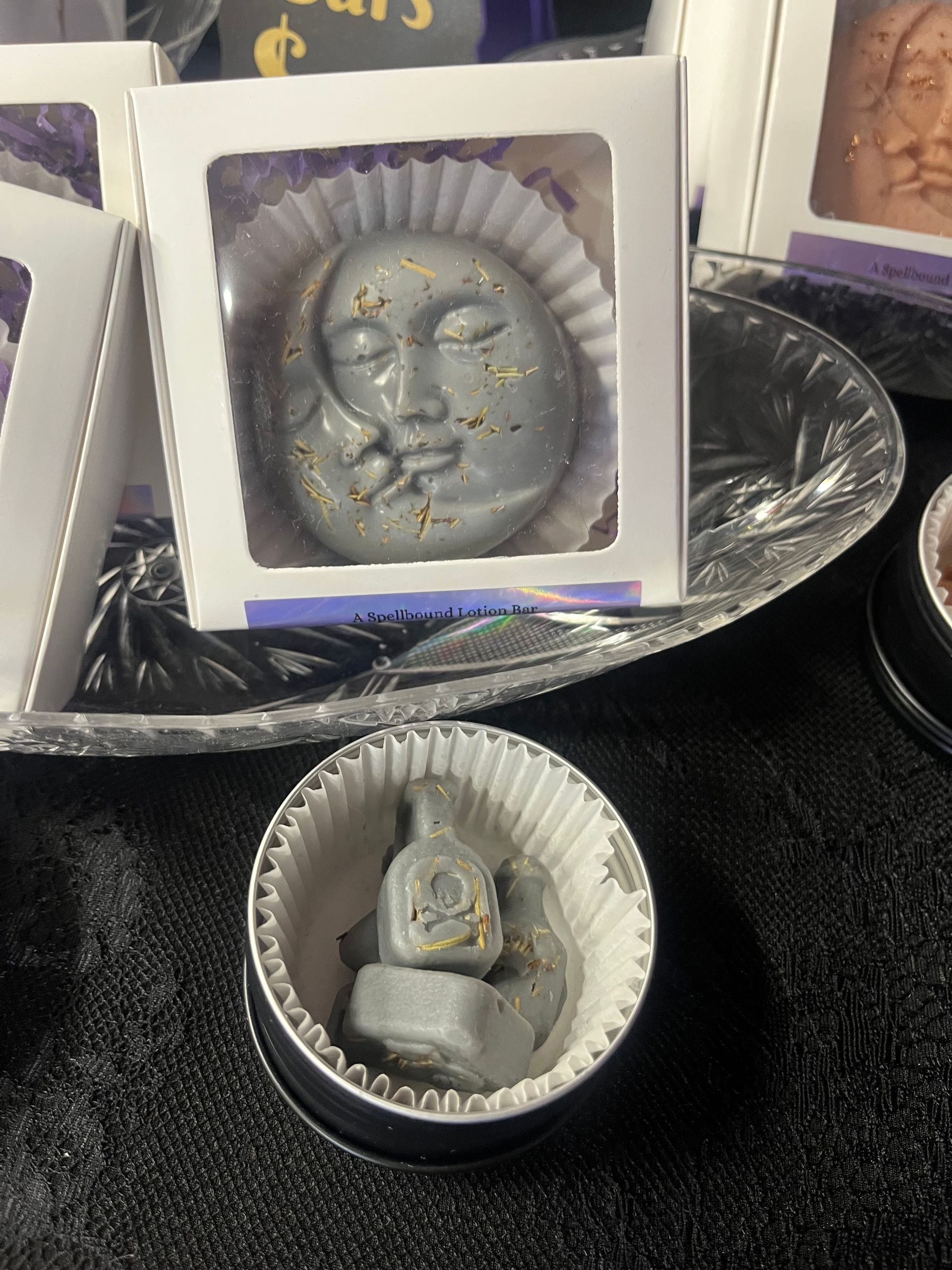 Silver Buddha face and small figurine in white gift boxes on a dark surface.