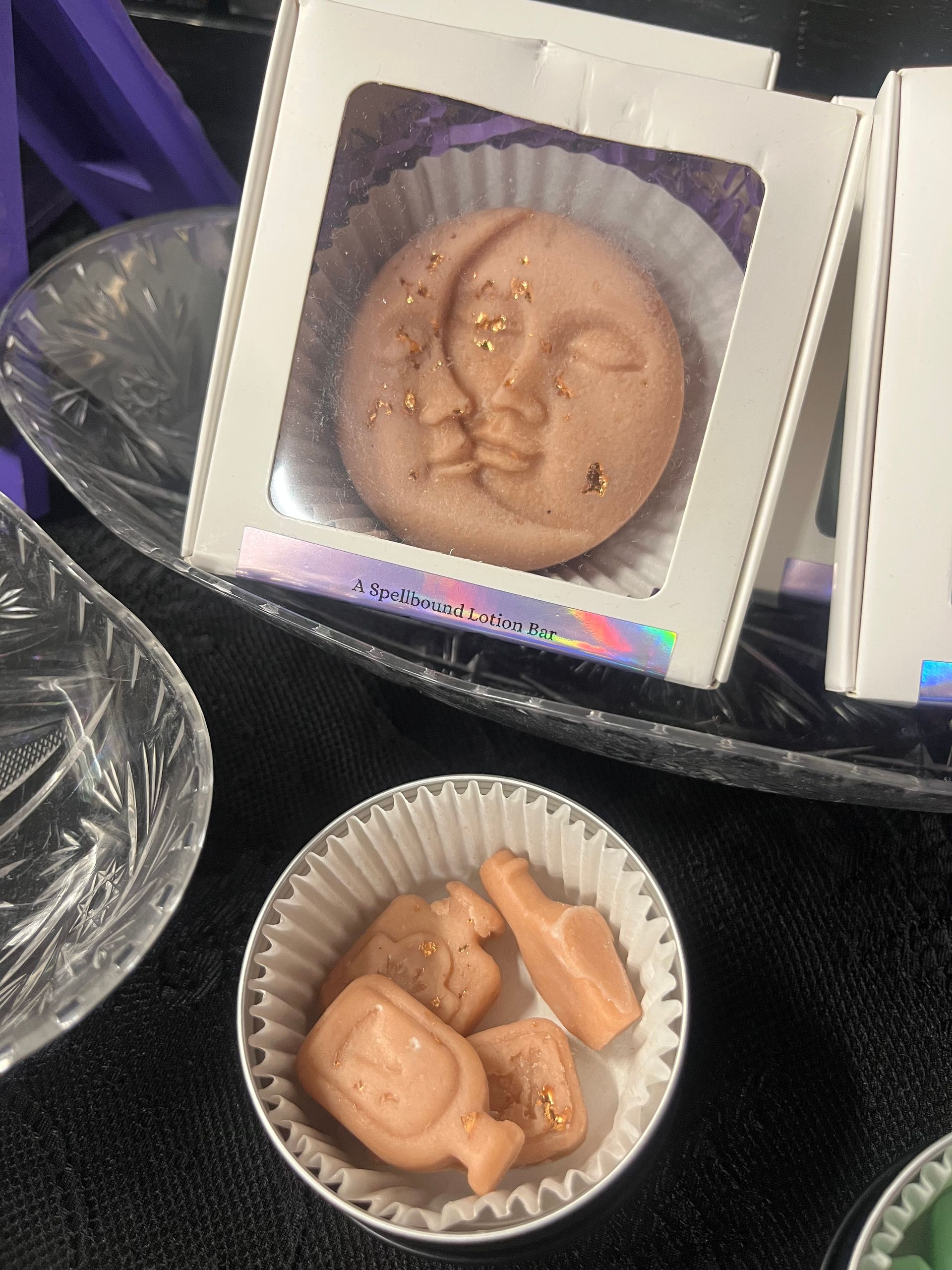 Round moon-face pastry in a white box beside a bowl of small peach-colored treats on a dark surface