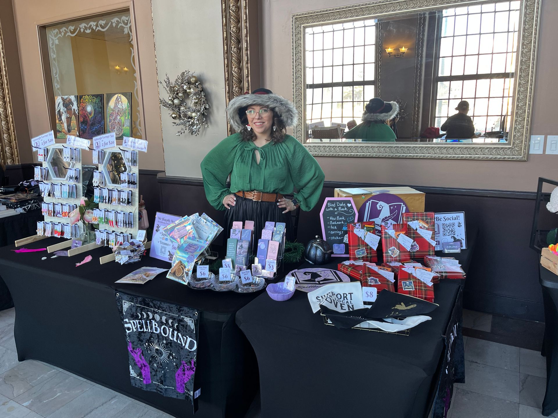 Vendor booth with a woman in green behind tables of colorful handmade crafts and gift items