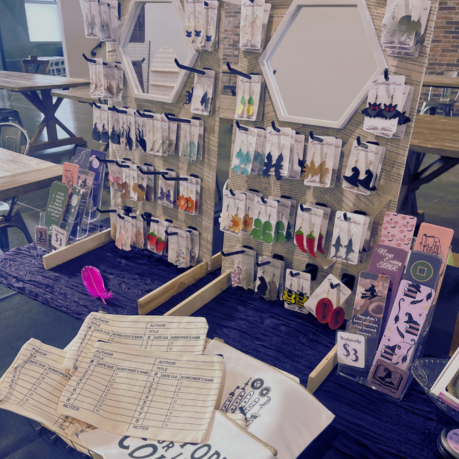 Craft display with hanging earrings and jewelry on a table, with cards and signs at an indoor market stall.
