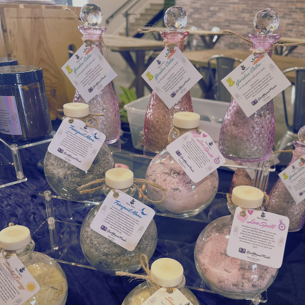 Gift baskets with pink bottles and candles arranged on a table with tags attached