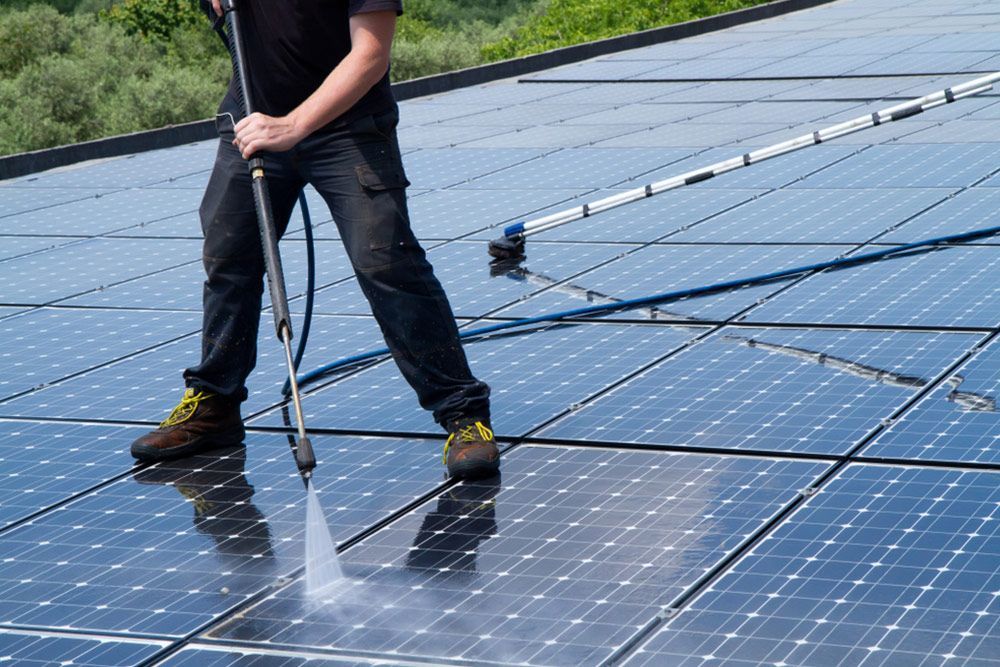 Man cleaning the solar panels using water pressure — Handyman in Ulladulla, NSW