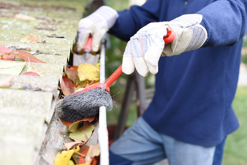 Man removing the dirt in the gutter using brush — Handyman in Nowra, NSW