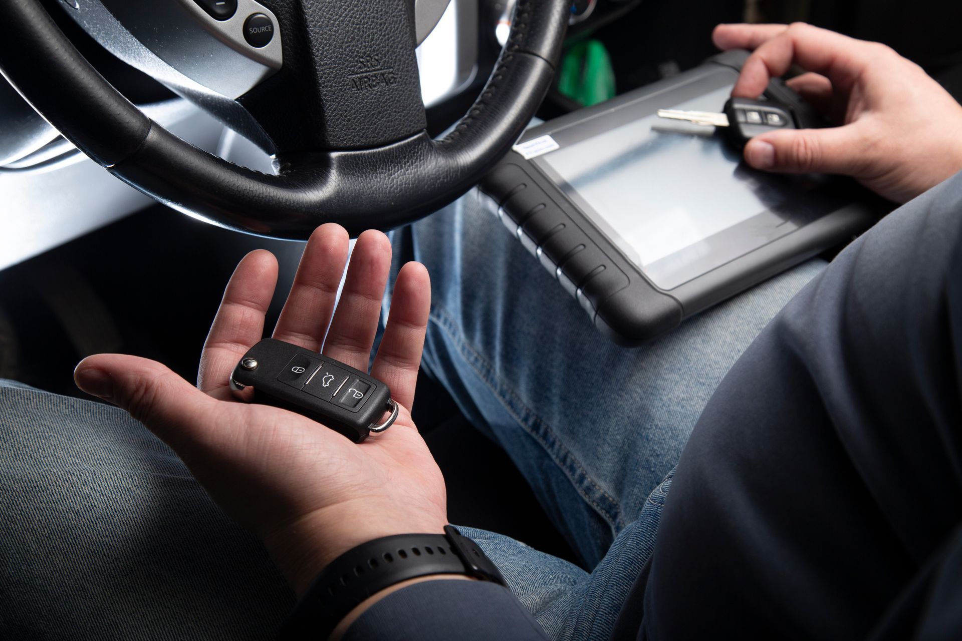 Close-up of a driver using a handheld device while seated in a car, with a steering wheel visible.