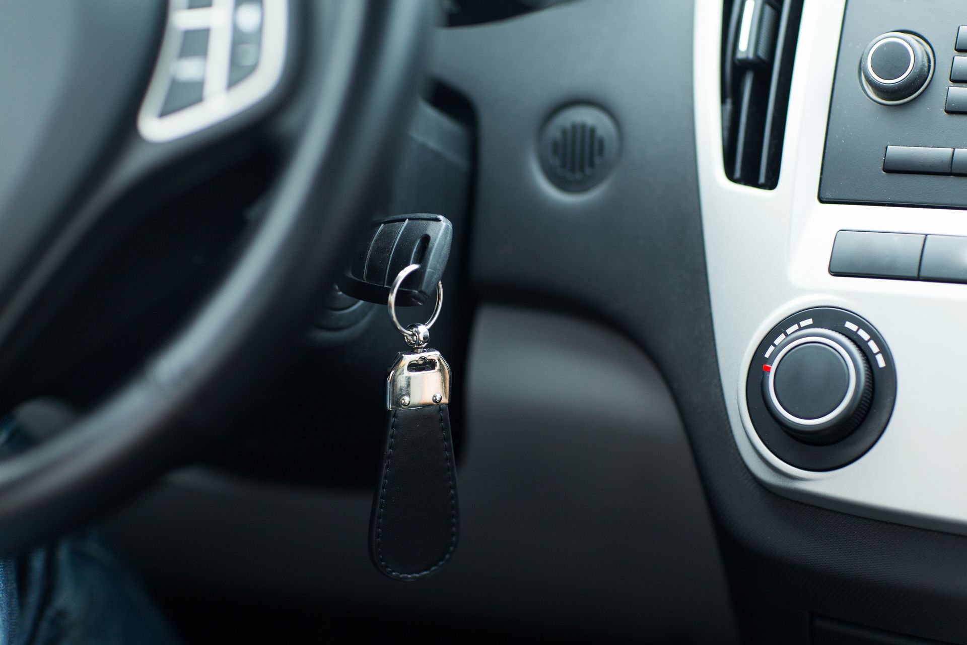 Car key dangling from the ignition in a car’s dashboard area. Car key dangling from the ignition in a car’s dashboard area.