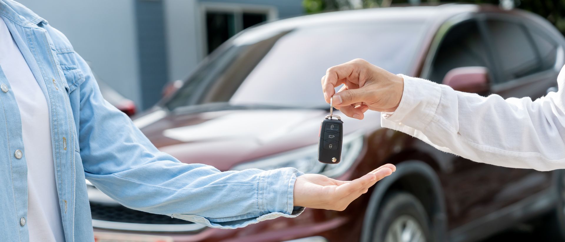 Keys being handed over beside a red car at a dealership.