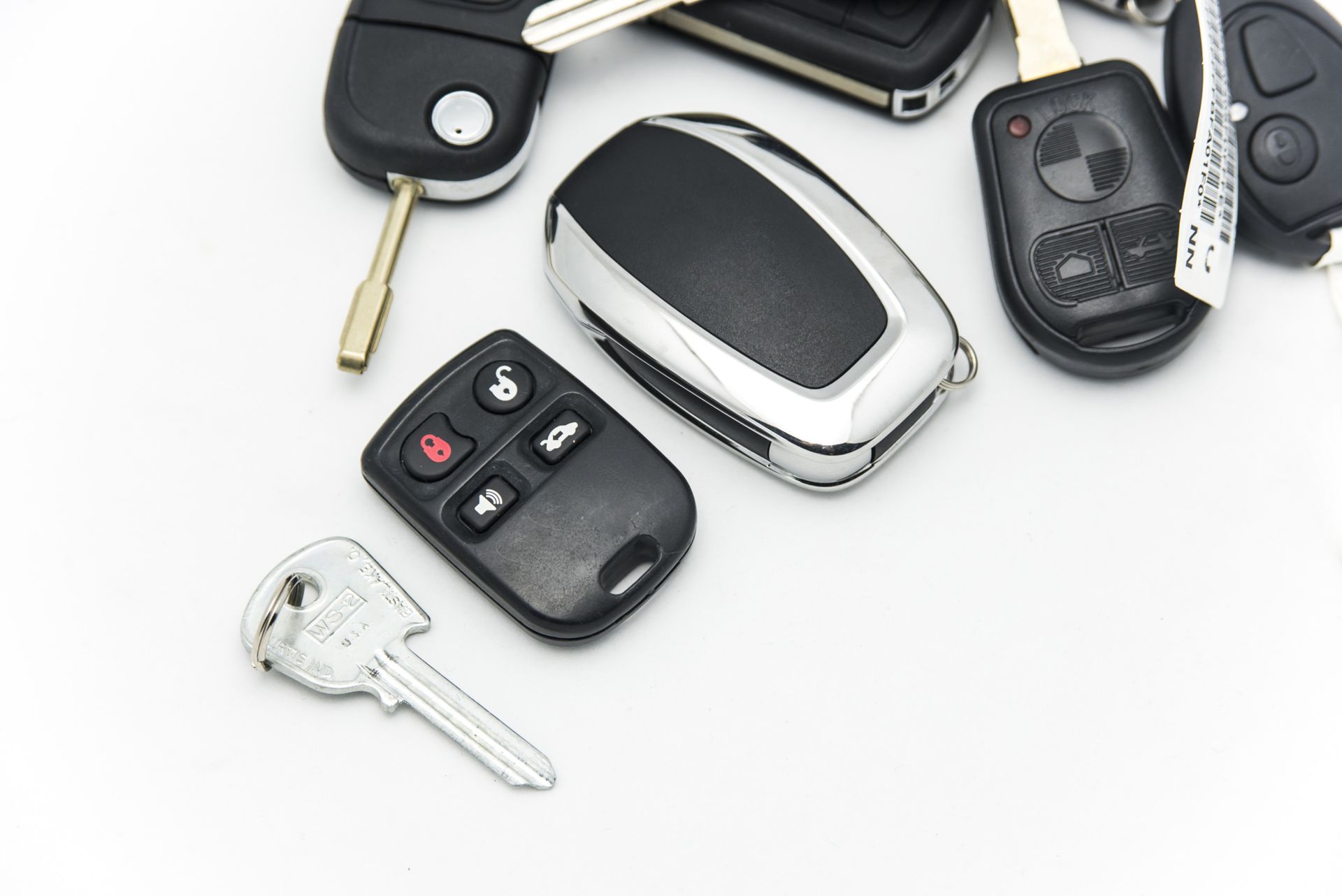 Assorted car keys and key fobs scattered on a white background.