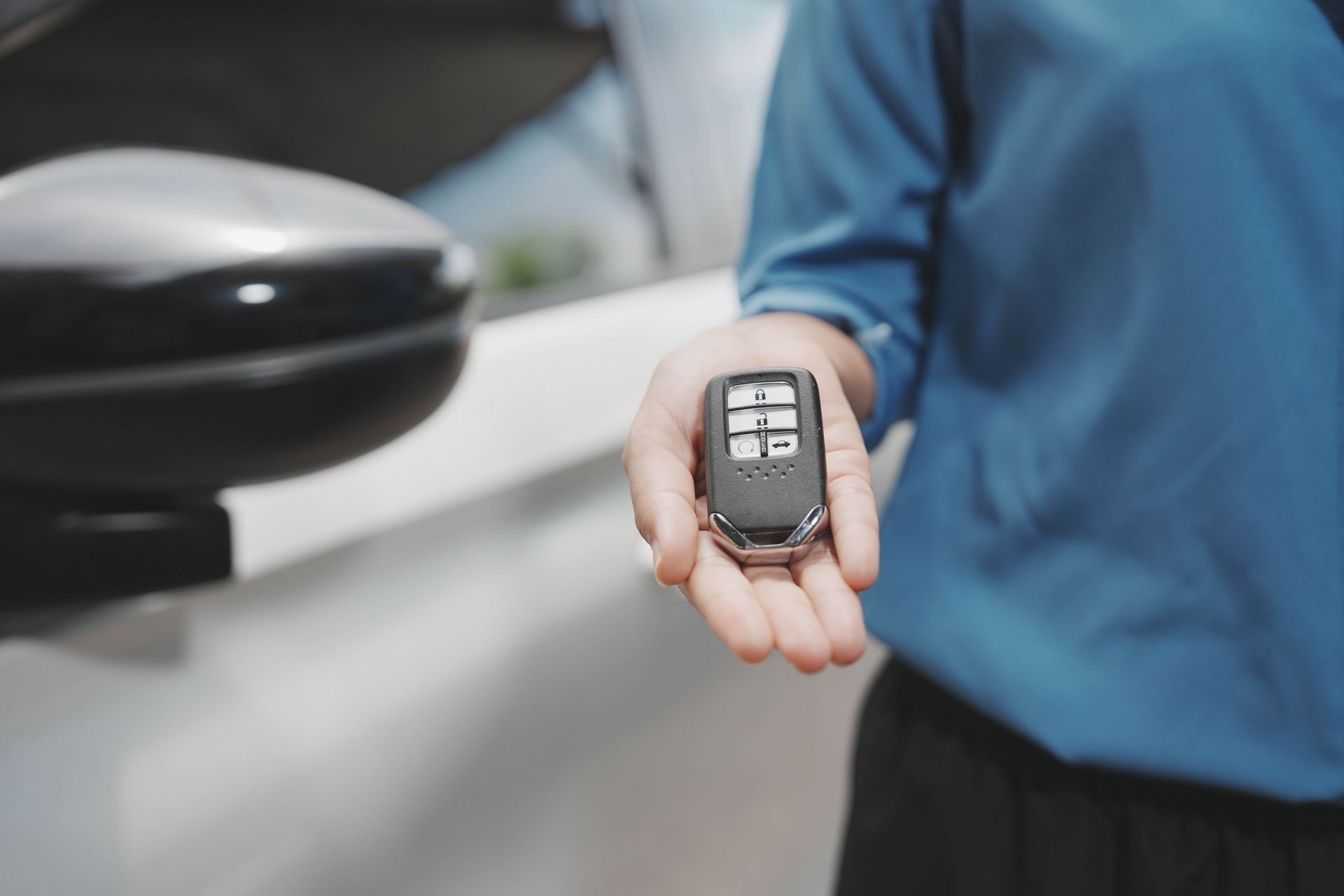 Person holding a car key fob beside a silver car door. Person holding a car key fob beside a silver car door.