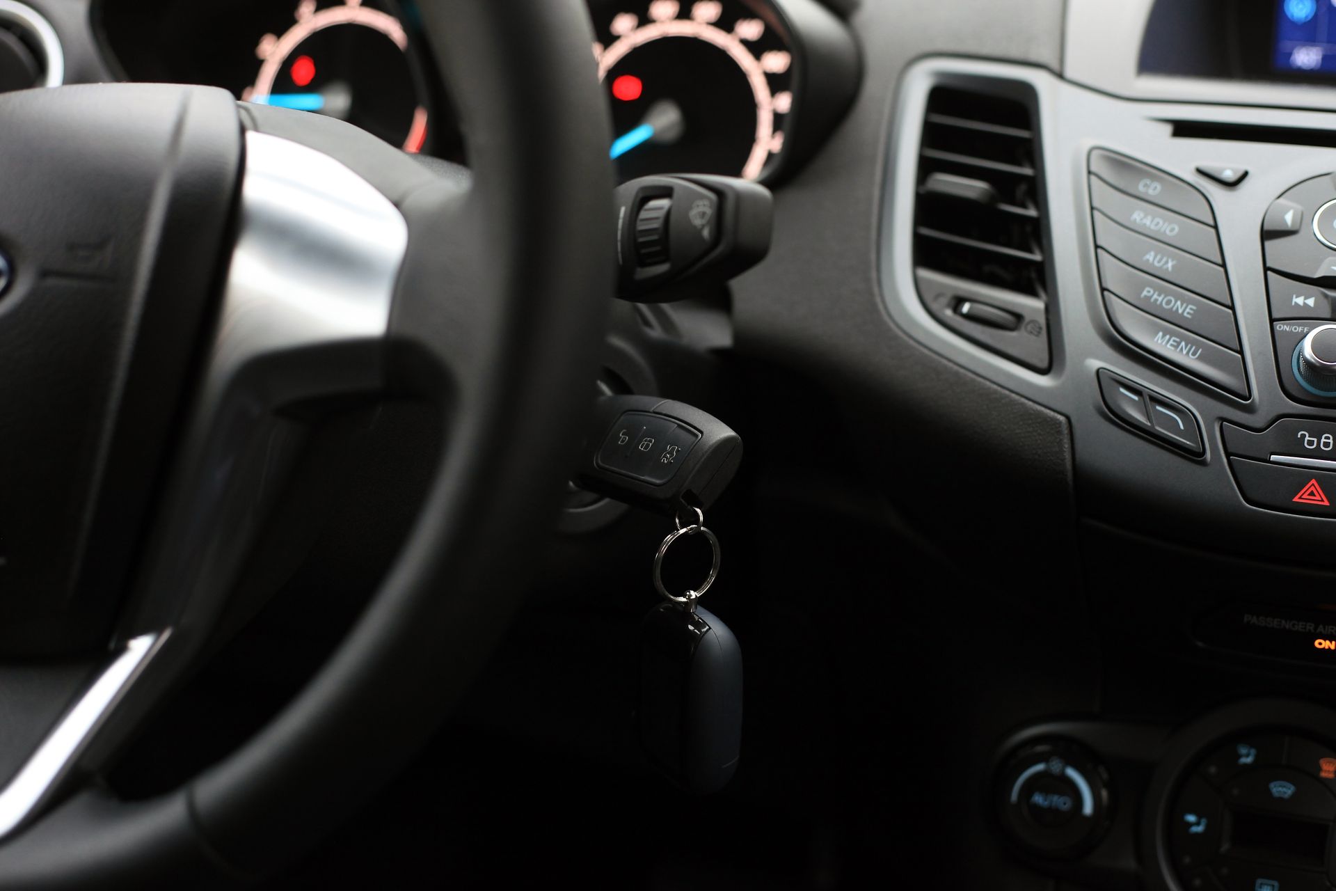 Car interior with steering wheel, dashboard gauges, center vents, and keys in the ignition. Car interior with steering wheel, dashboard gauges, center vents, and keys in the ignition.