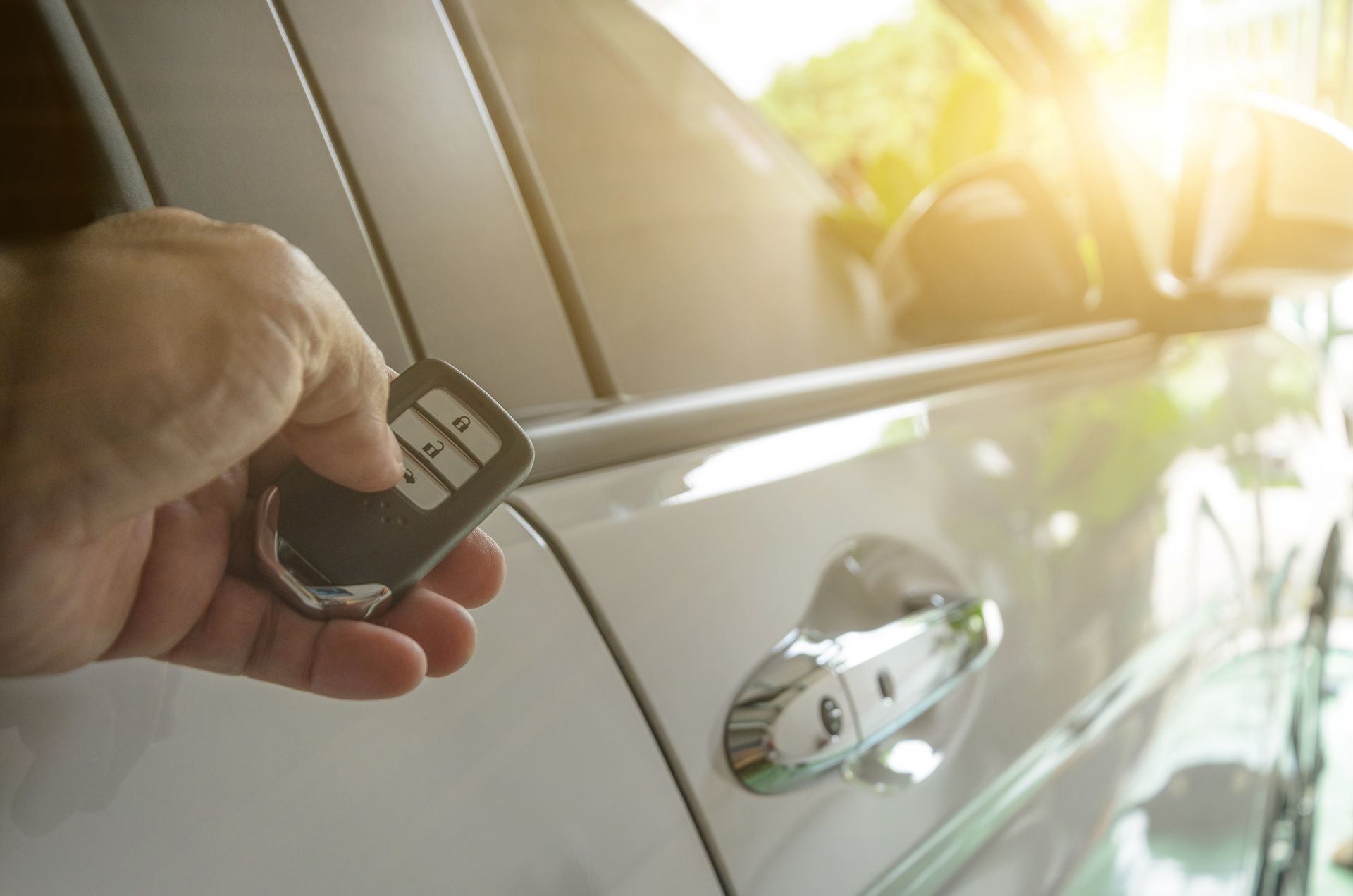 Hand holding car key fob near white car door handle in sunlight. Hand holding car key fob near white car door handle in sunlight.
