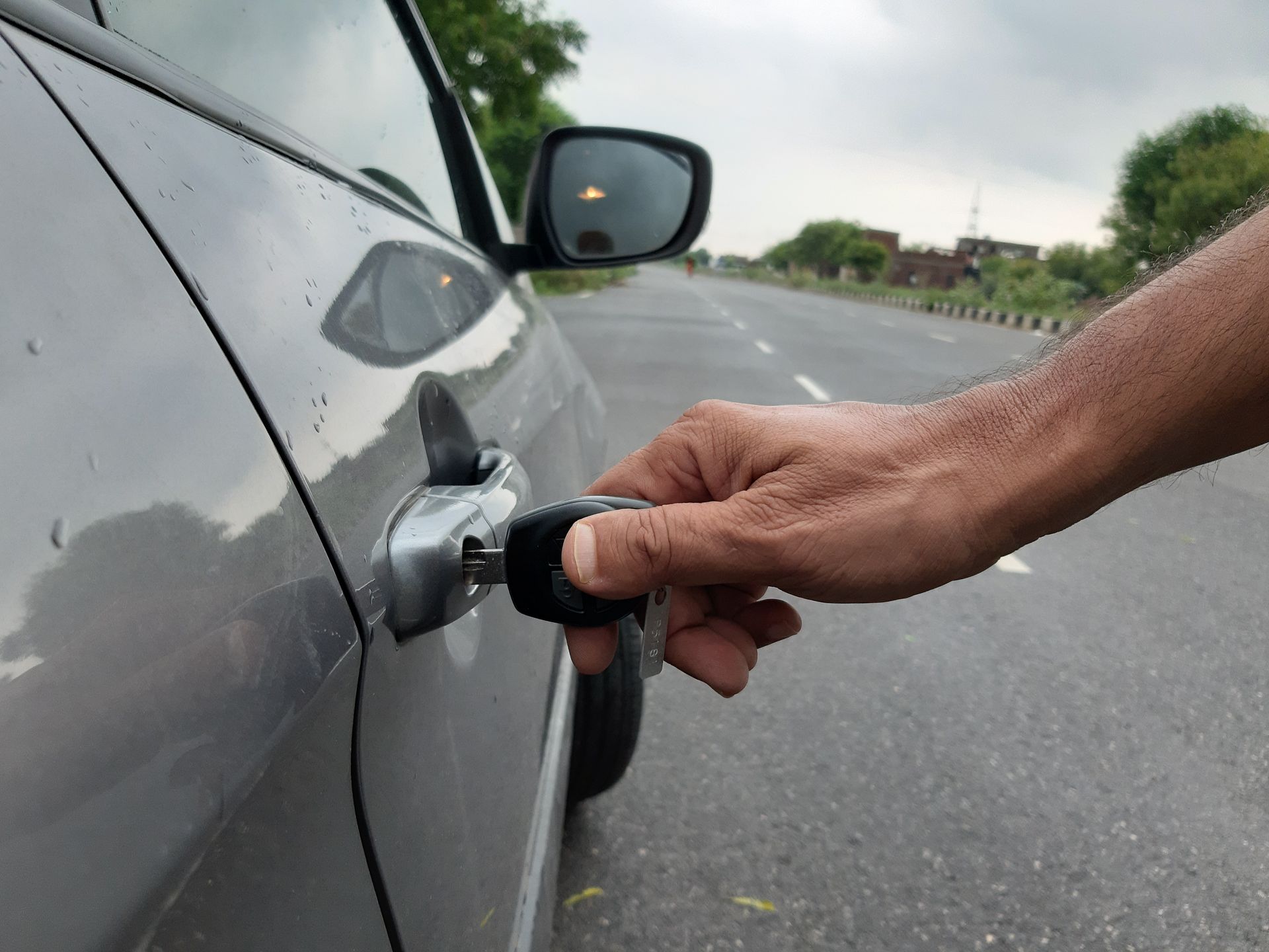 Hand gripping a car’s fuel nozzle while refueling a gray vehicle on a roadside. Hand gripping a car’s fuel nozzle while refueling a gray vehicle on a roadside.