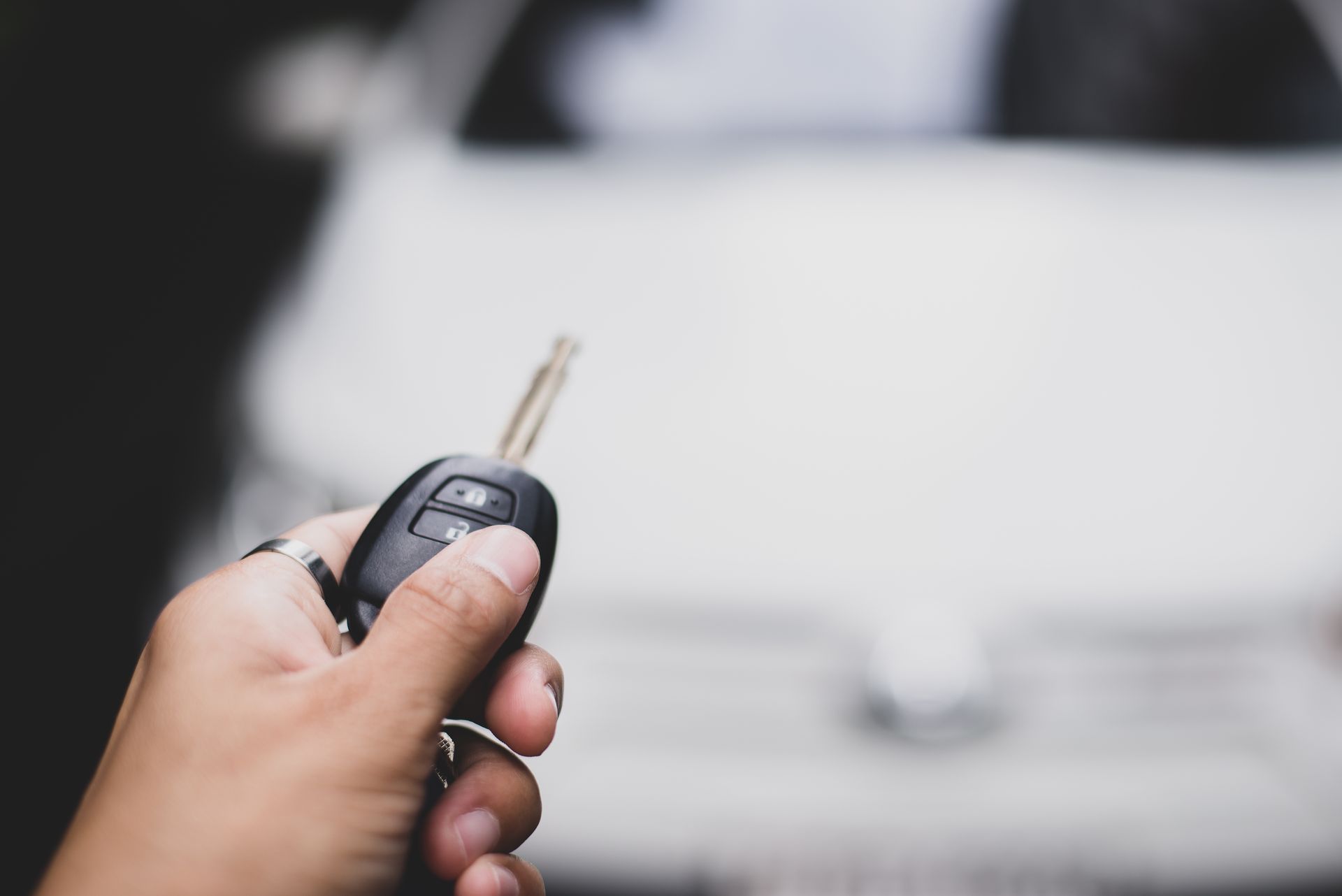 Hand holding a car key fob in front of a blurred white car. Hand holding a car key fob in front of a blurred white car.