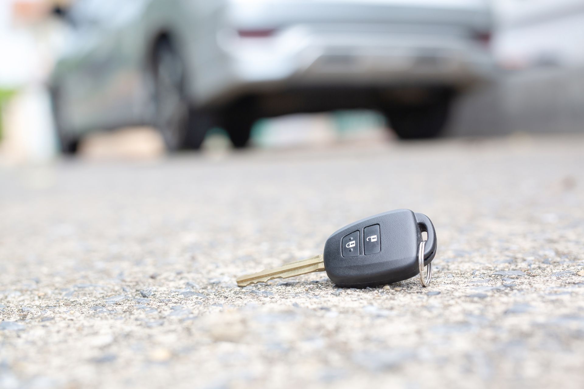 Car key lying on the road near a blurred car in the background. Car key lying on the road near a blurred car in the background.