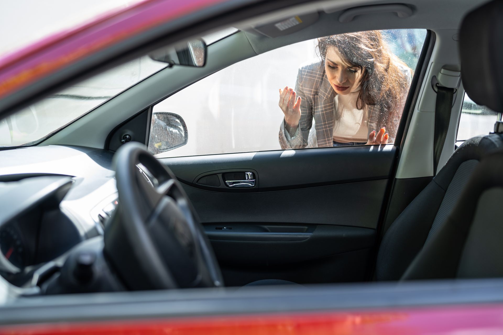 Woman looking into a red car through the passenger window. Woman looking into a red car through the passenger window.