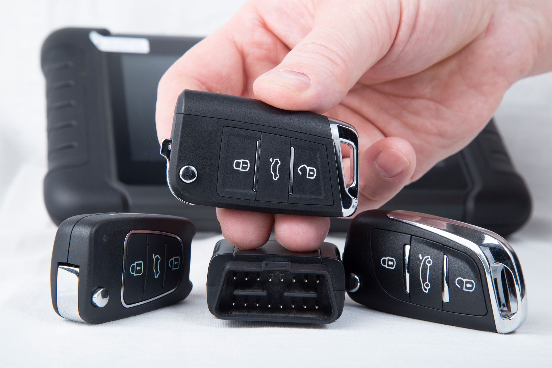 Hand holding a black car key fob above three other key fobs on a white background. Hand holding a black car key fob above three other key fobs on a white background.