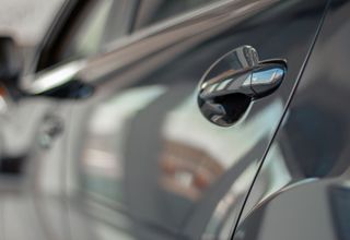 Close-up of a gray car door and chrome handle, with a blurred reflection on the glossy surface.