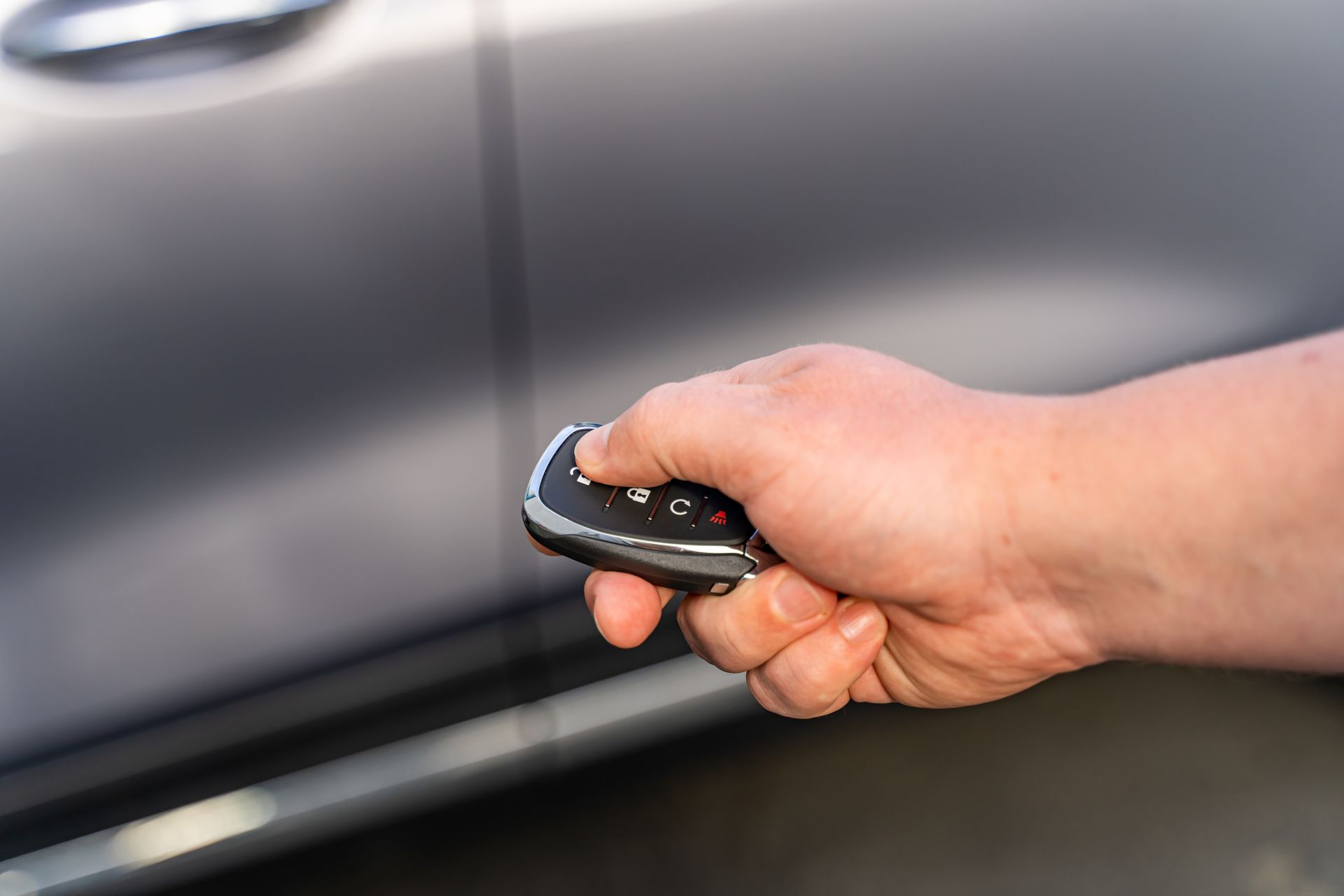 Hand opening a car door with a black key fob near a gray vehicle panel. Hand opening a car door with a black key fob near a gray vehicle panel.