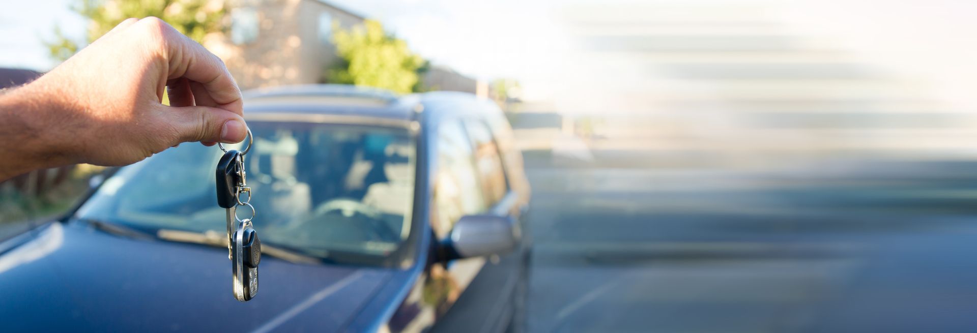 Hand holding car keys in front of a blue car on a road. Hand holding car keys in front of a blue car on a road.