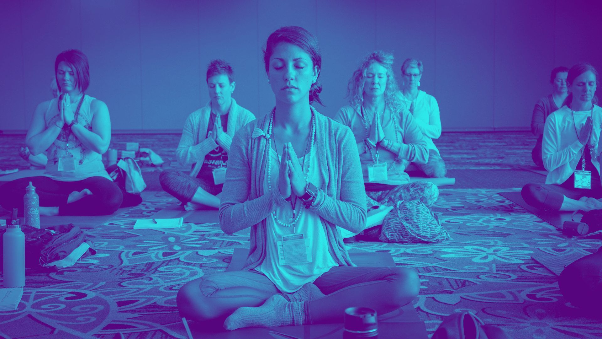 A group of people are sitting in a lotus position on a yoga mat.