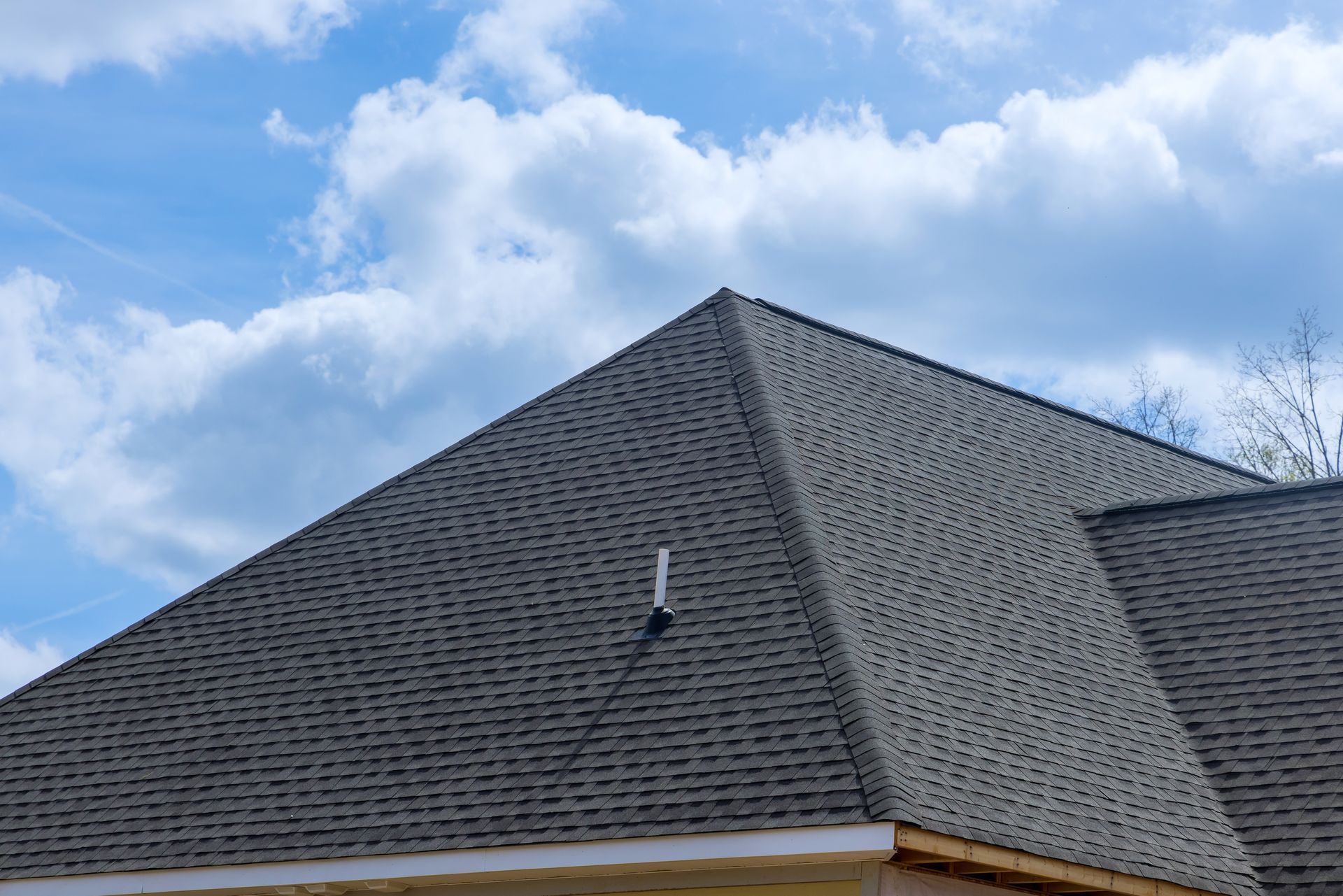 Gray shingled roof against a blue sky with fluffy white clouds.