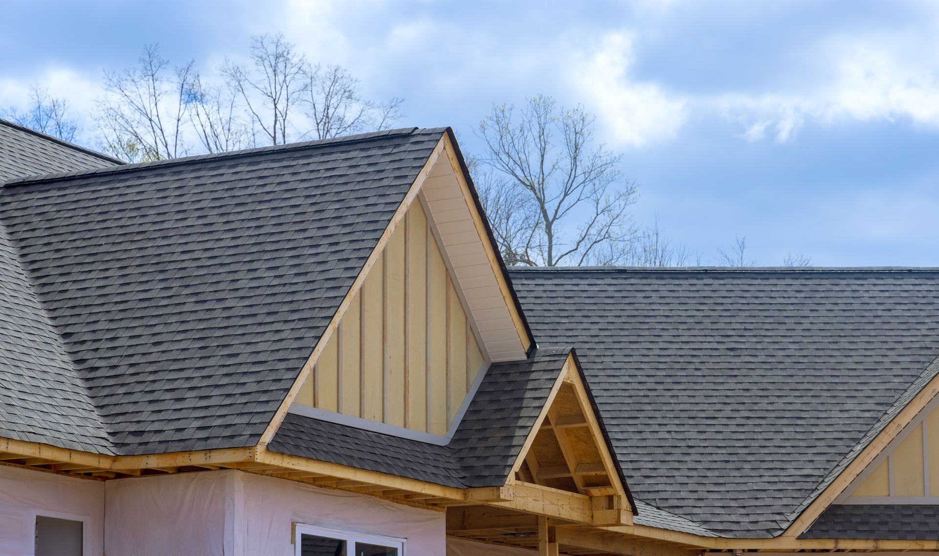 Construction of a new house roof with grey shingles and unfinished wooden structure against a cloudy sky.