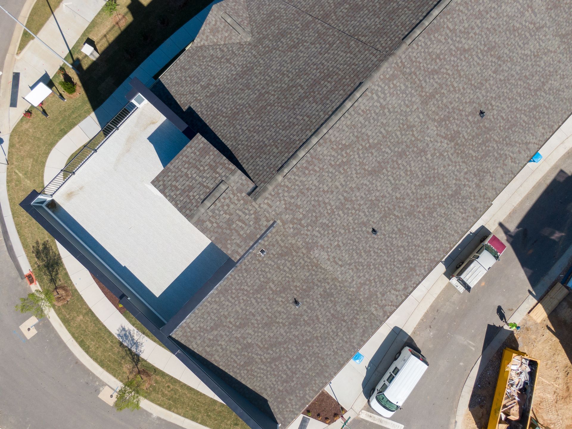 Aerial view of a building with a dark shingled roof, a white patio, and a curved street.