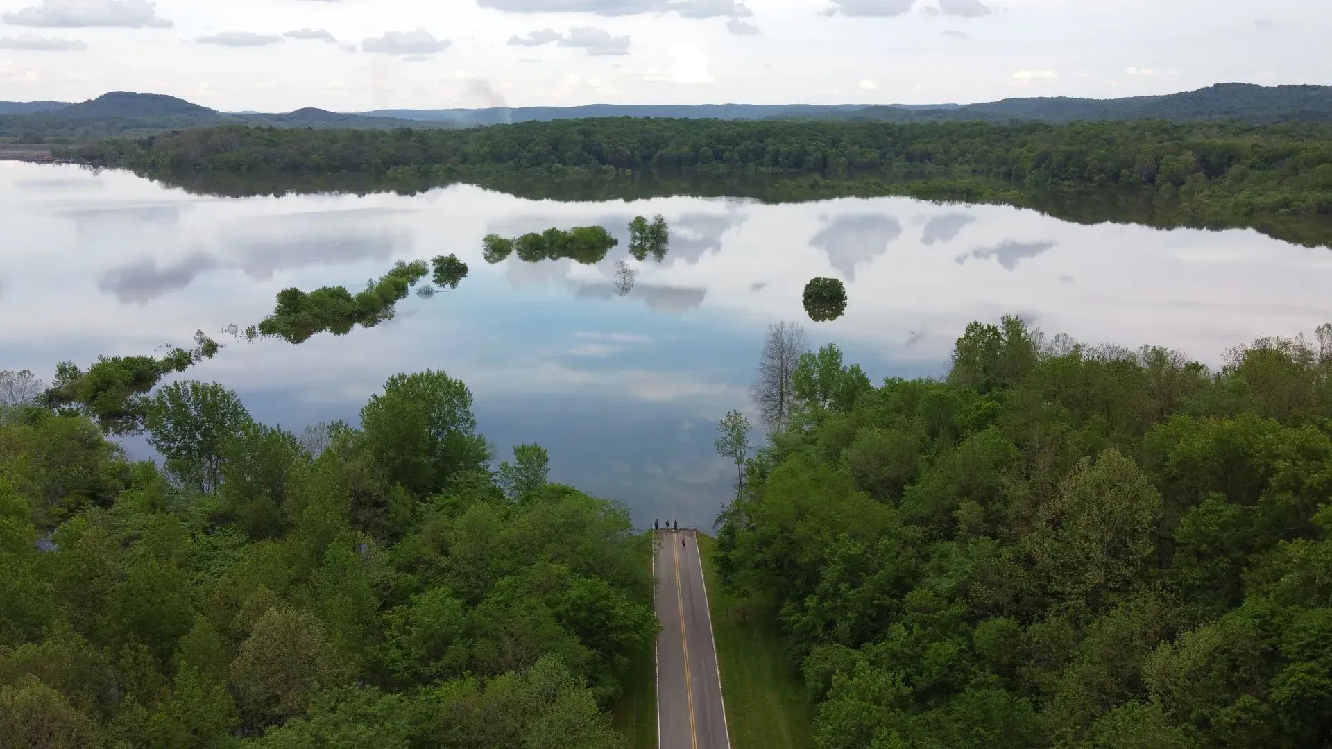 An aerial view of a road leading to a lake surrounded by trees.