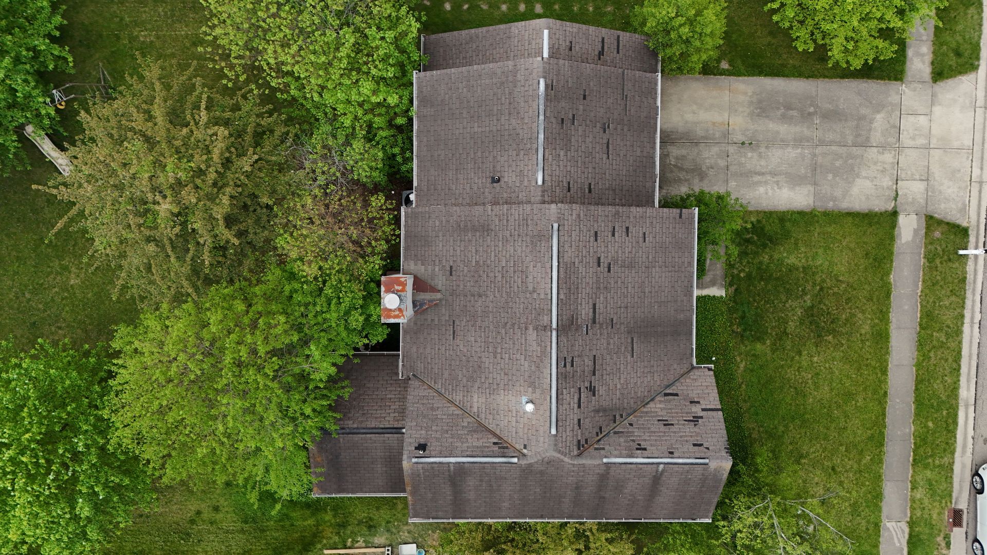An aerial view of a house with a roof that is surrounded by trees. Inspected by drone.