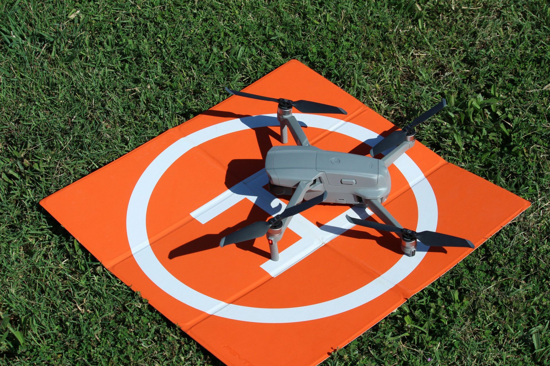 Drone on an orange and white landing pad on a grassy field.