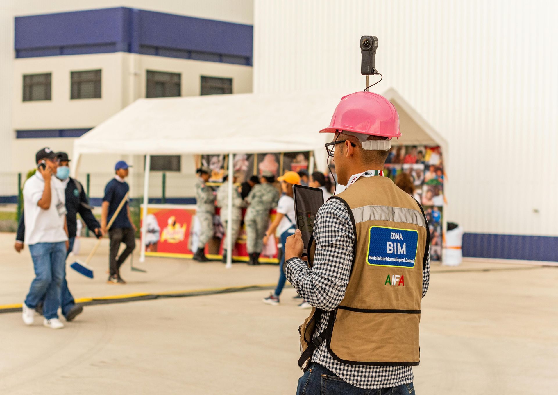 Person wearing pink hard hat and vest with camera on head, surveying an event.