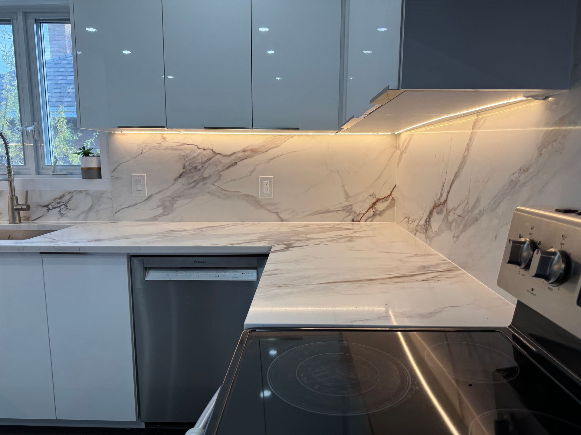 A kitchen with a stove , sink , dishwasher and marble counter tops.