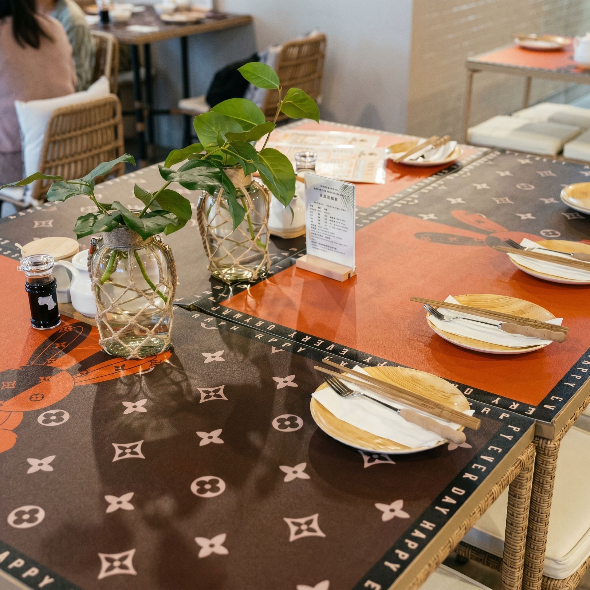 Set dining table with sushi plates, potted plants, and orange-and-brown patterned tablecloth in a restaurant