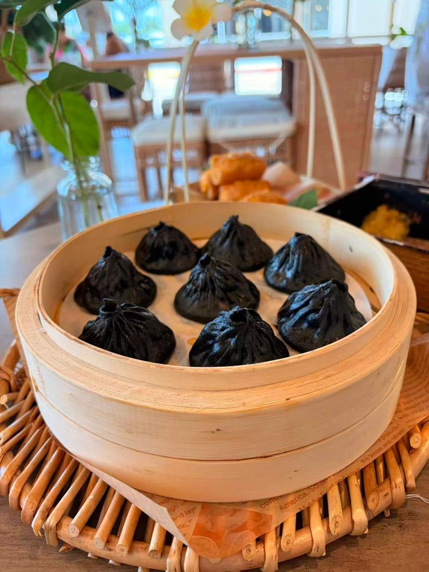 Braised meat garnished with chopped red chilies in a brass serving bowl on a wooden table