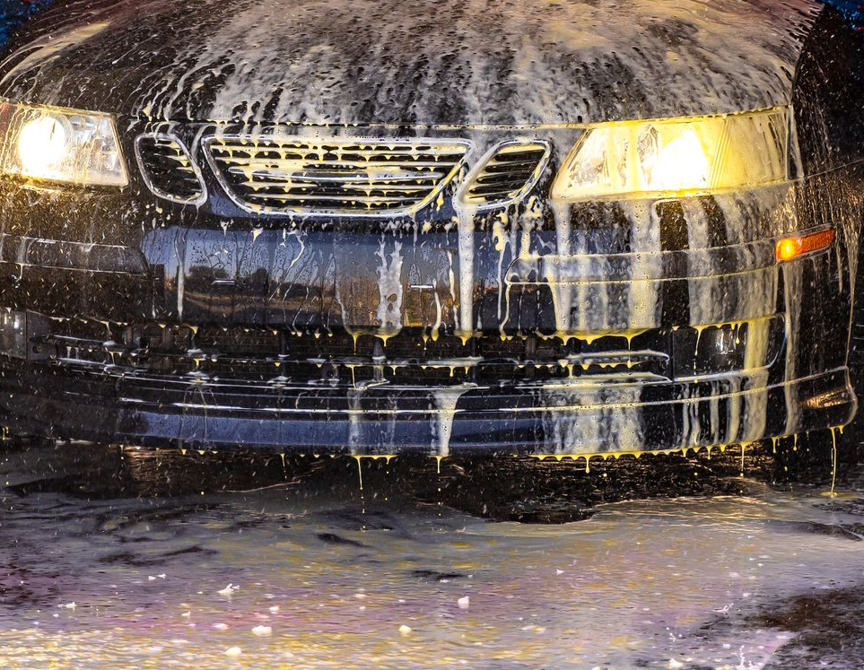 Car being washed in an automatic car wash; blue and red brushes, soapy water, and bright lights. Car being washed in an automatic car wash; blue and red brushes, soapy water, and bright lights.