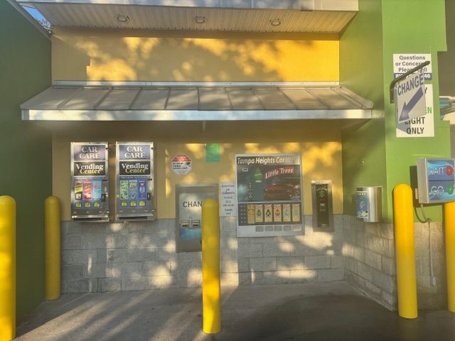 Drive-thru car wash entrance with yellow and green accents, featuring payment kiosks and signs.