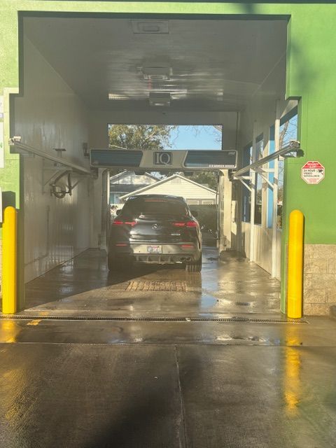 Black car inside a car wash bay with green walls and yellow poles.