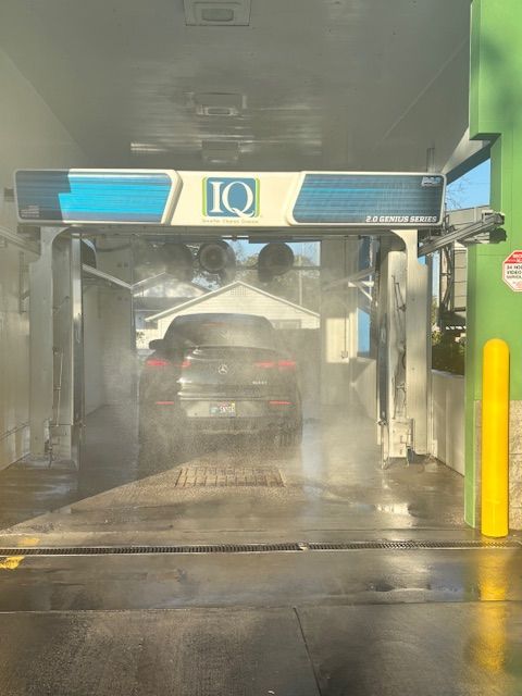 A car inside a car wash, surrounded by mist and water.