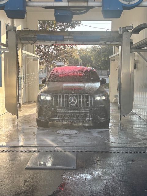 Silver car being washed in a carwash; water sprays, red brushes. Silver car being washed in a carwash; water sprays, red brushes.