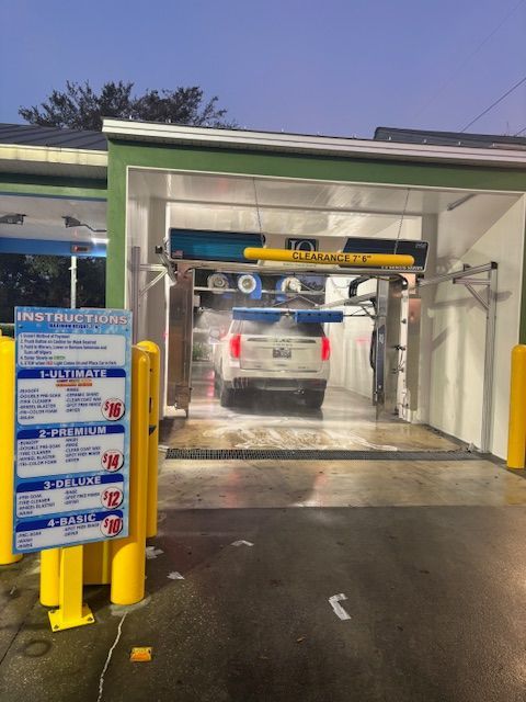 Car wash: a white SUV inside. Foam spraying, with price list on the left and wash opening above.
