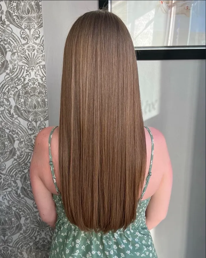 Back view of long straight light brown hair, reaching mid-back, against an indoor patterned wall.