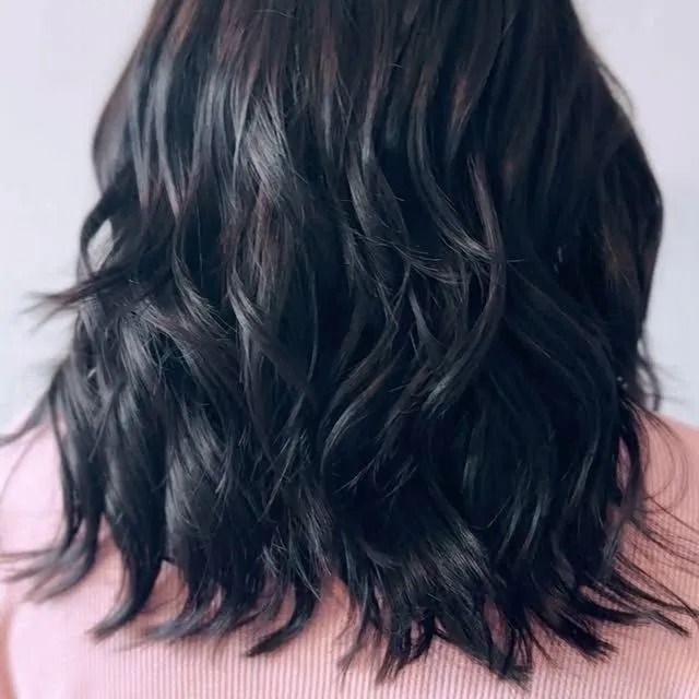 Wavy dark shoulder-length hair viewed from the back on a light pink background