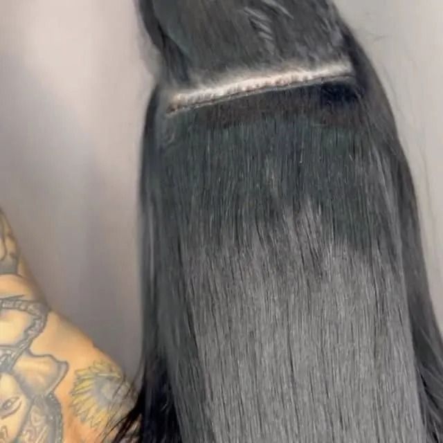 Close-up of long straight black hair with a silver hair clip, with a tattooed arm at the edge