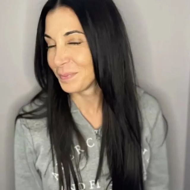 Smiling person with long black hair wearing a gray sweatshirt against a plain light background