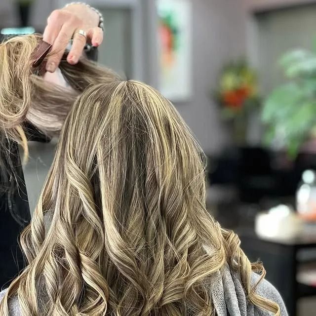 Close-up of blonde, highlighted hair being styled in a salon with curls and a stylist’s hand visible