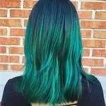 Back view of shoulder-length teal-to-black ombré hair against a brick wall