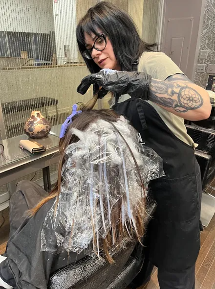 Hair stylist dyeing a client’s hair in a salon, with foil and color brush visible.